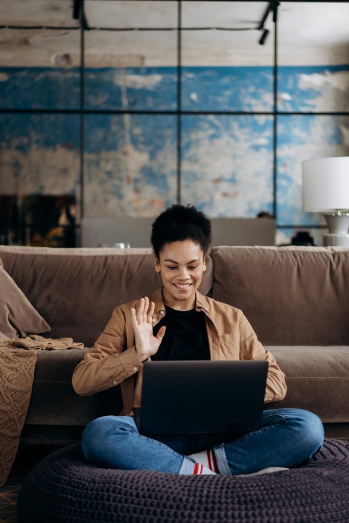 Man in Brown Dress Shirt and Blue Denim Jeans Sitting on Brown Couch Using Black Laptop